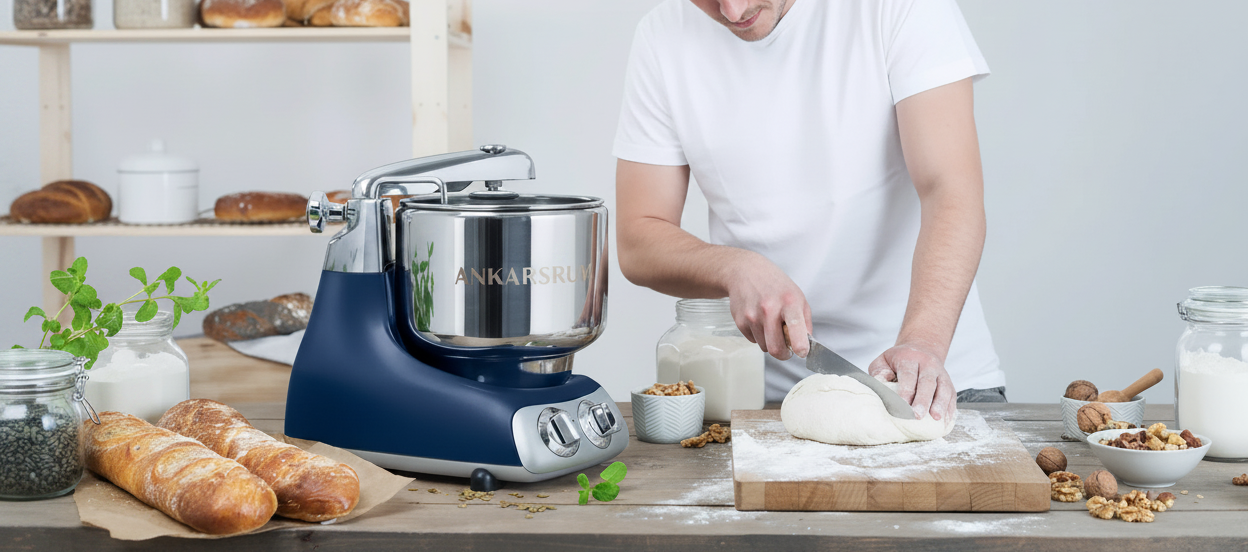 Blue Ankarsrum stand mixer on a kitchen counter with a person kneading dough.